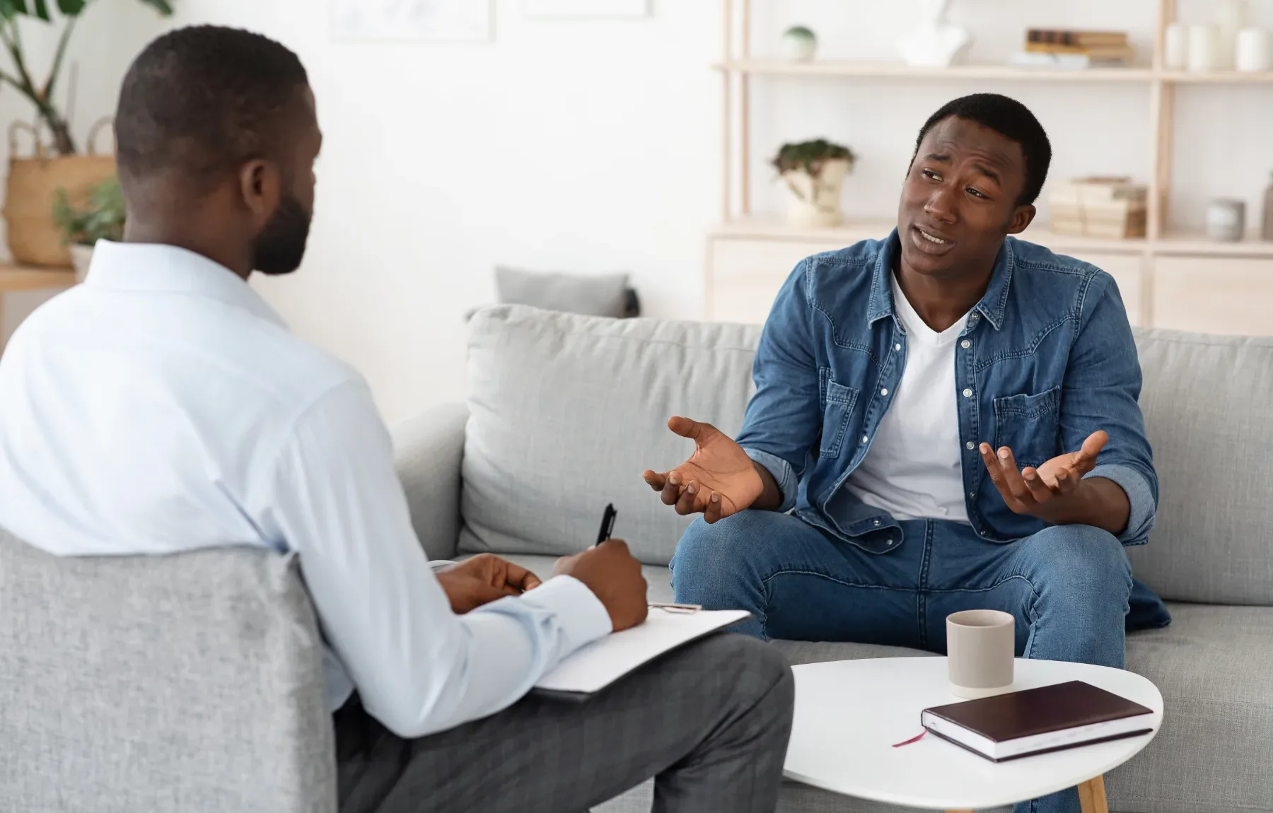 Male therapist taking notes while listening to patient during a counseling session in a comfortable office setting
