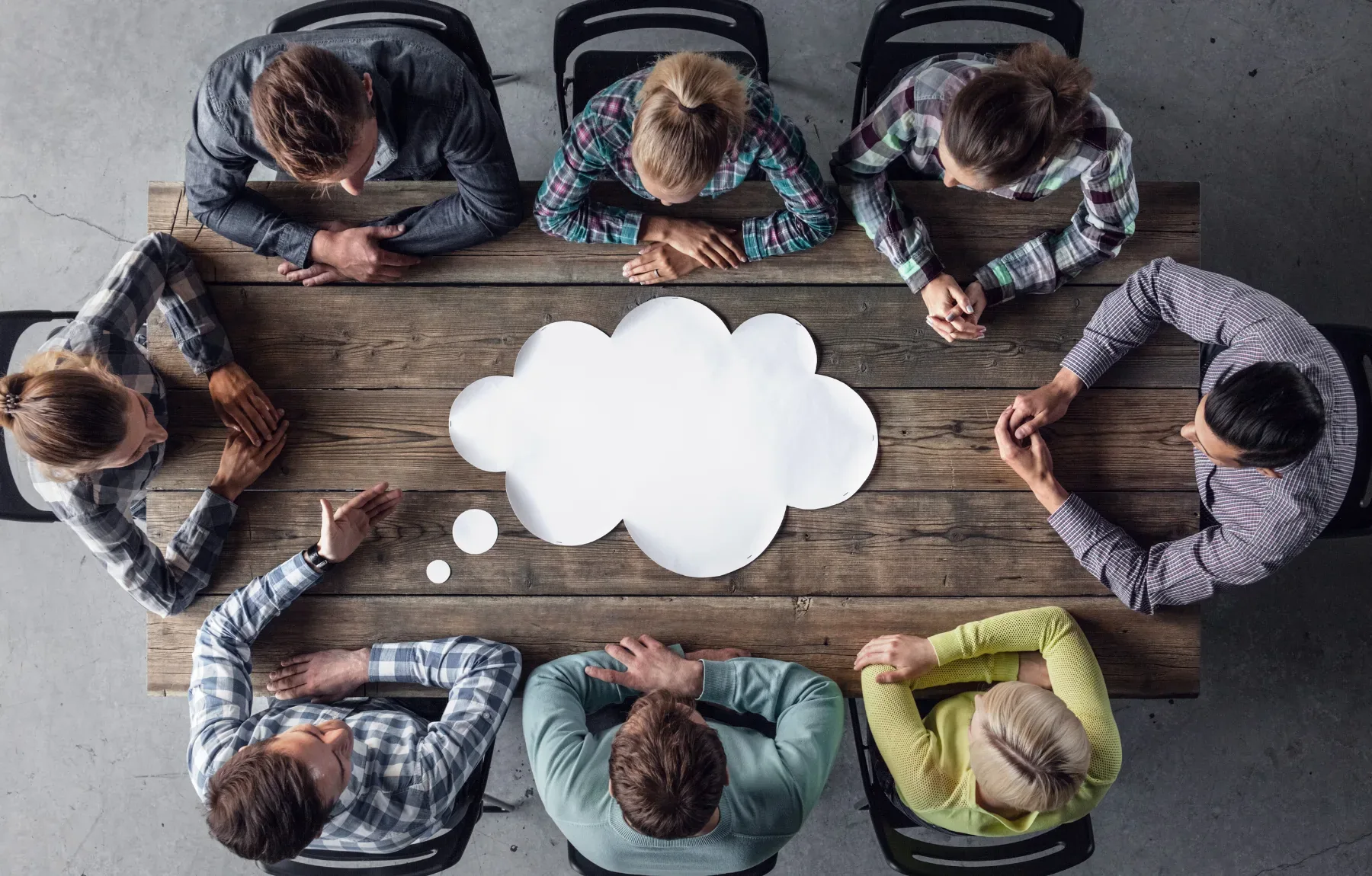 Overhead view of diverse group of people sitting in circle around white thought bubble, symbolizing therapy, counseling, grou
