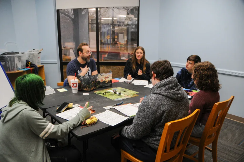 Six people seated around a table playing a board game during a group therapy session.