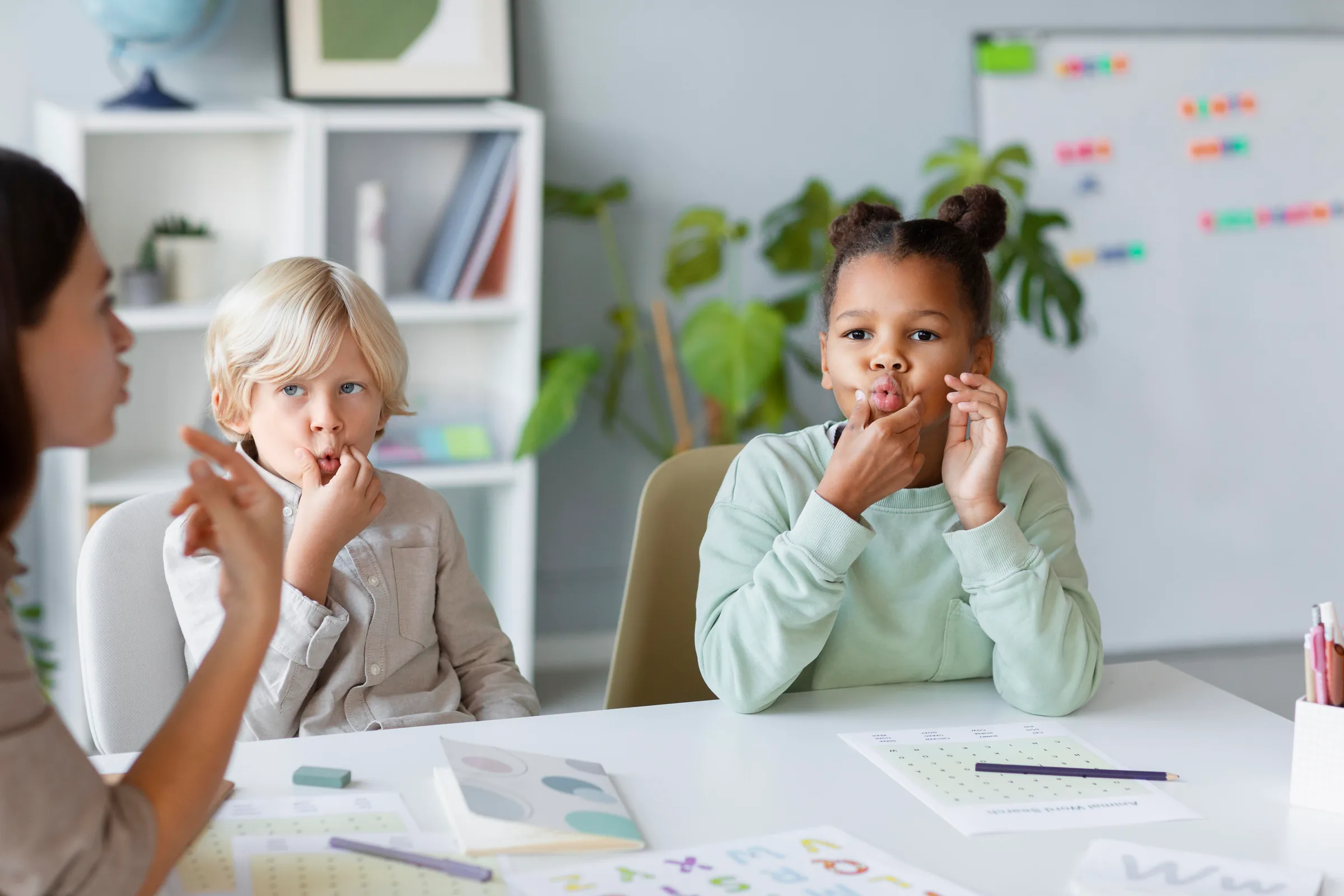 Speech pathologist working with two young children on articulation exercises in a bright therapy room.
