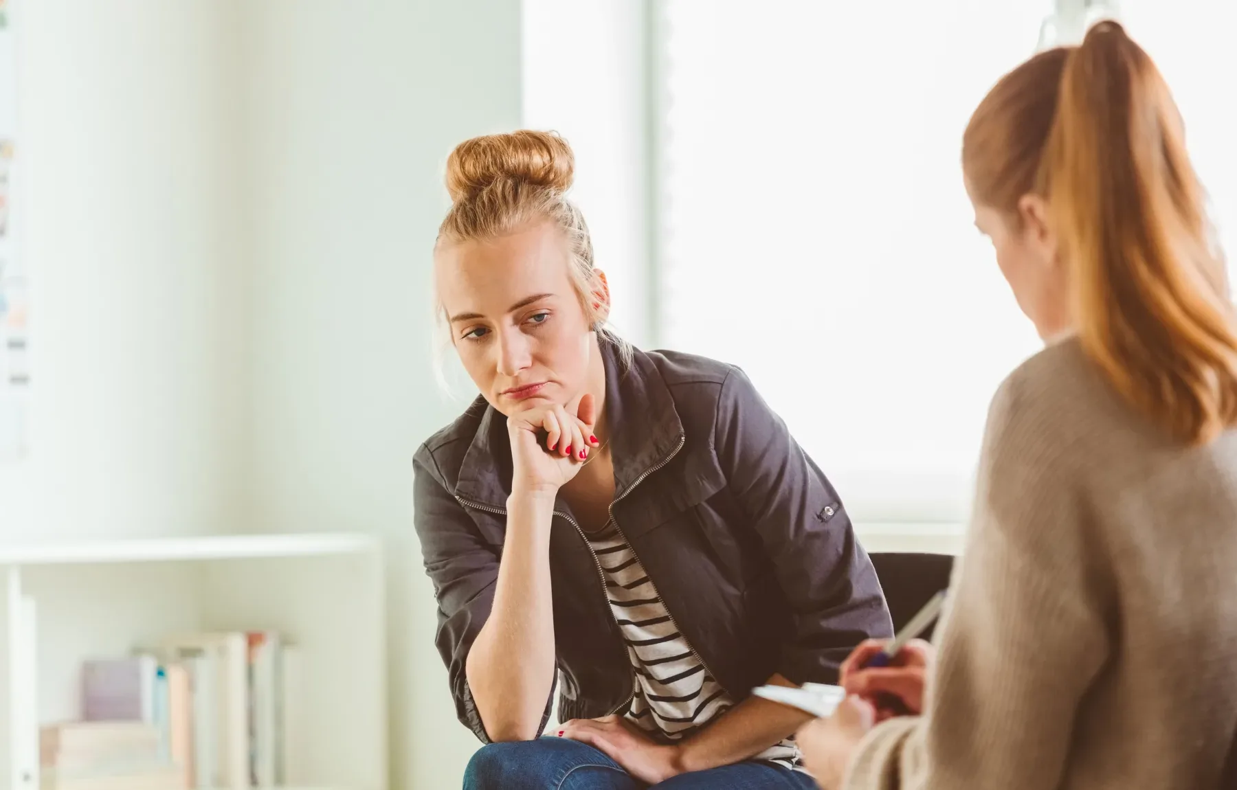 A therapist listens attentively to a client during a counseling session in a bright, modern office setting.